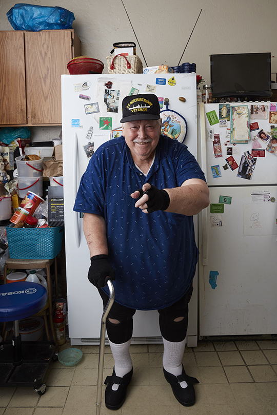 Veteran standing in his home's kitchen smiling and pointing to the camera