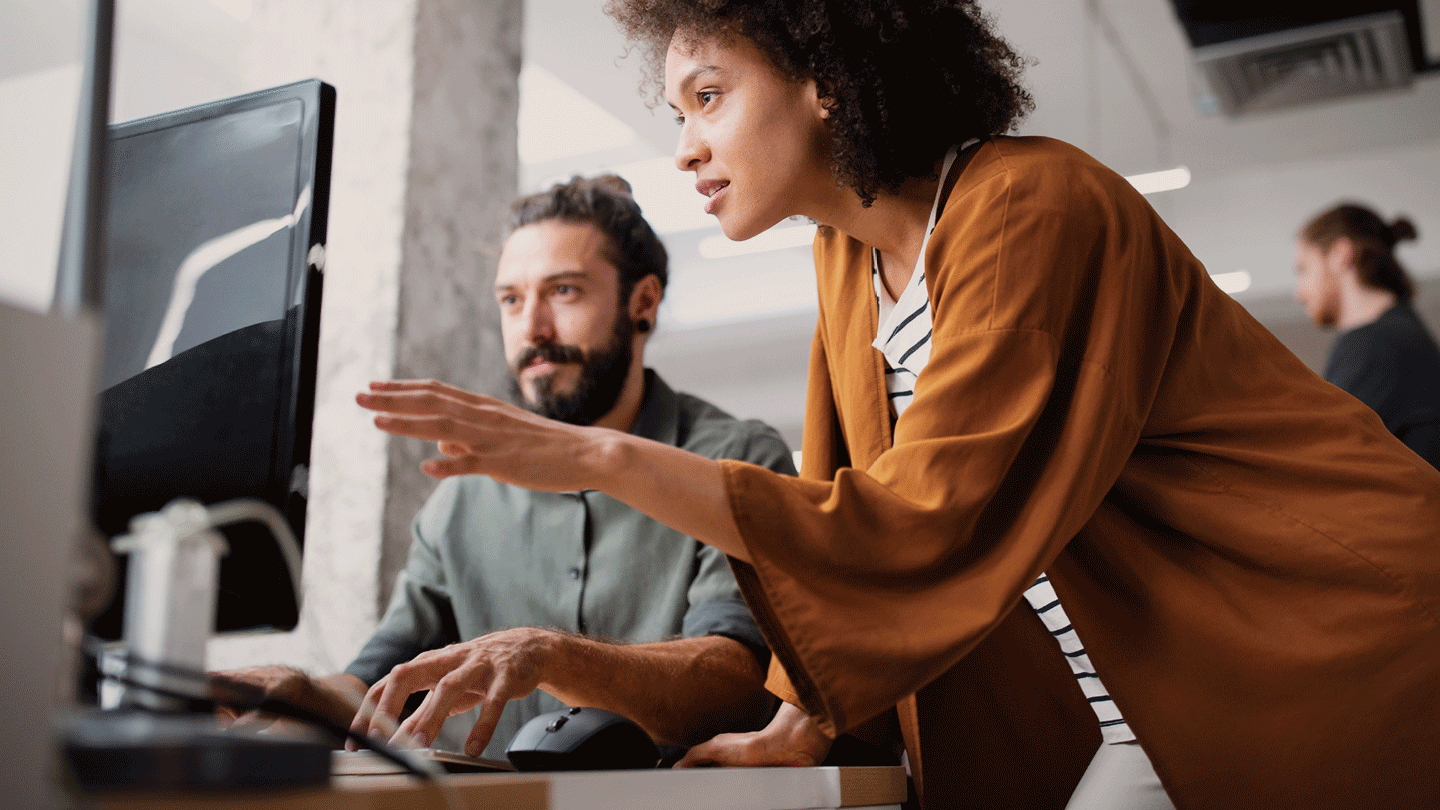 Two people working at a desk and looking at a computer monitor together