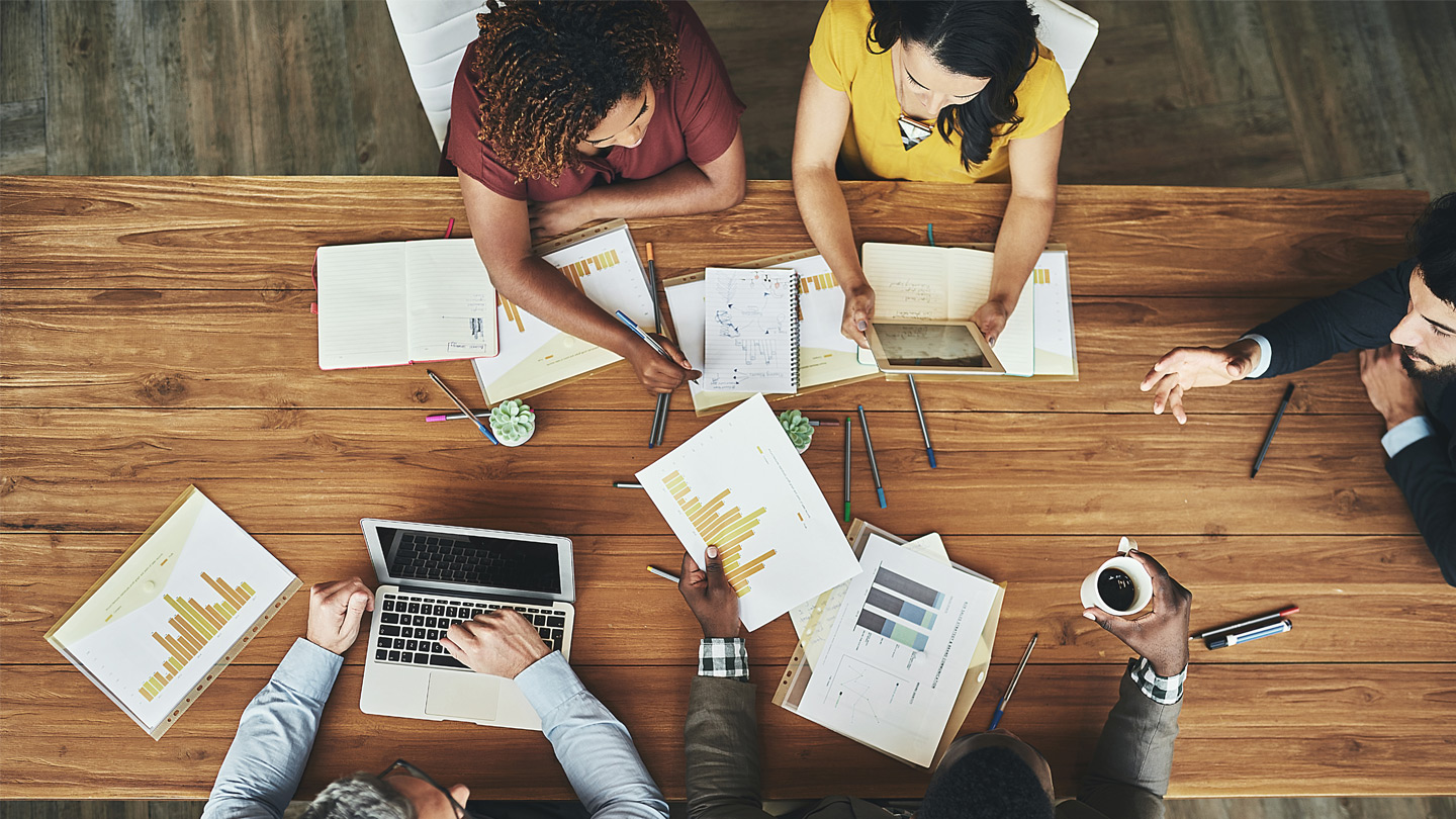 Aerial view of a group sitting around a conference table looking at graphs and charts