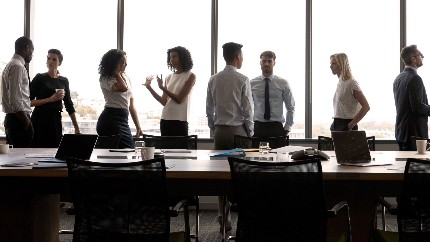 Group of people standing in conference room talking to one another