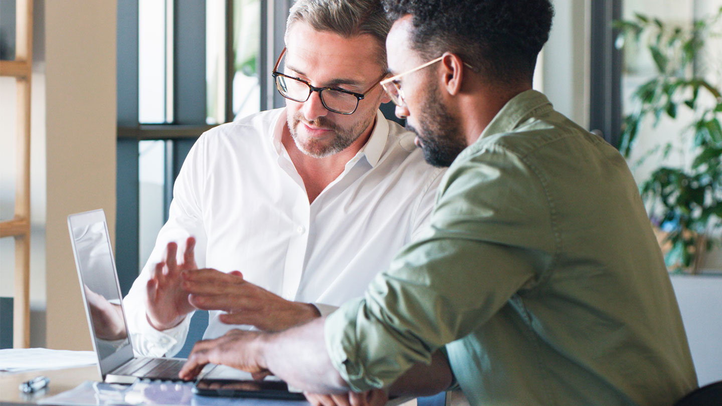 Two people talking and working around a laptop