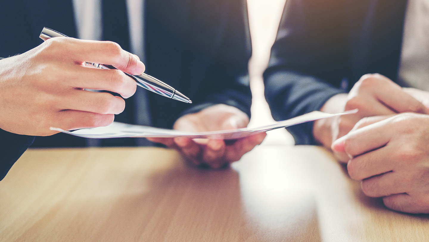 Two sets of hands holding a paper and pen at a desk