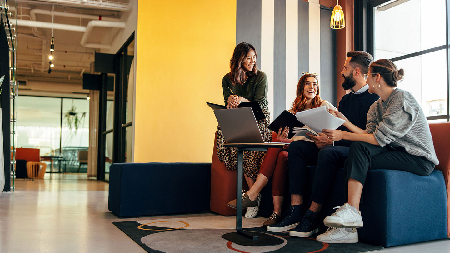 Multicultural businesspeople working in an office lobby. Group of happy businesspeople smiling while sitting together in a co-working space. Young entrepreneurs collaborating on a new project.