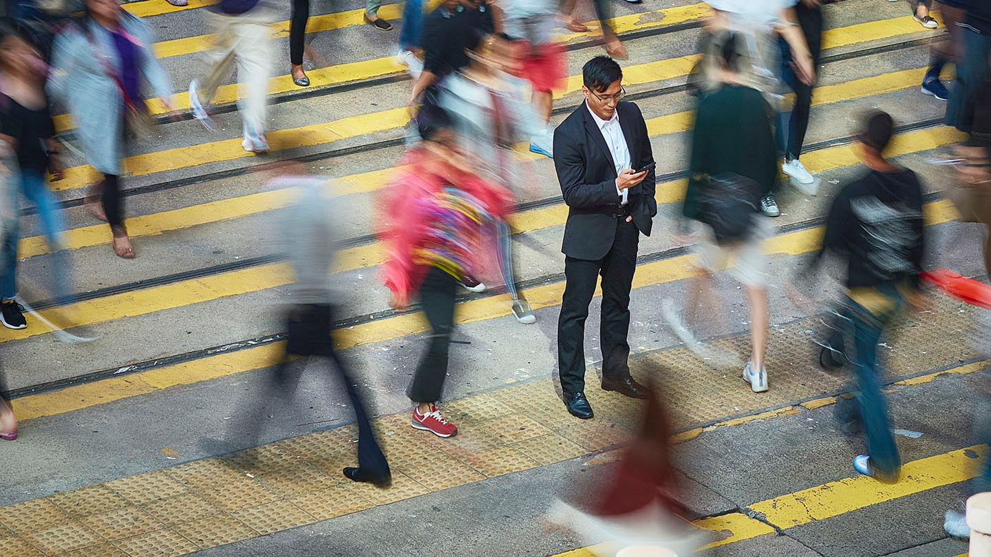 High angle view of businessman using smart phone amidst crowd. Professional is standing on busy street. He is surrounded by people in city.