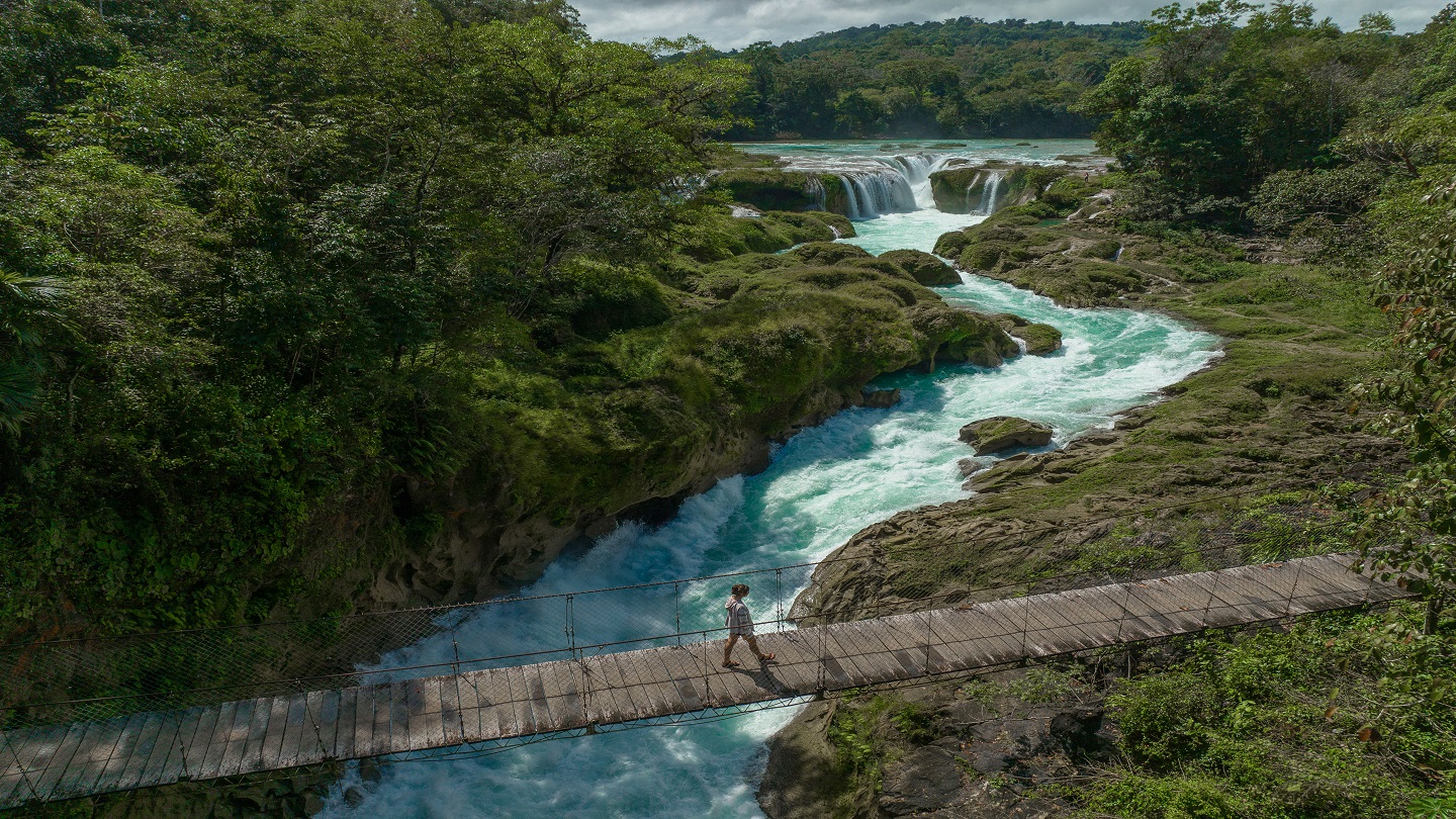 Scenic aerial view of  woman walking on suspension bridge over  Las Nubes waterfall in Chiapas
