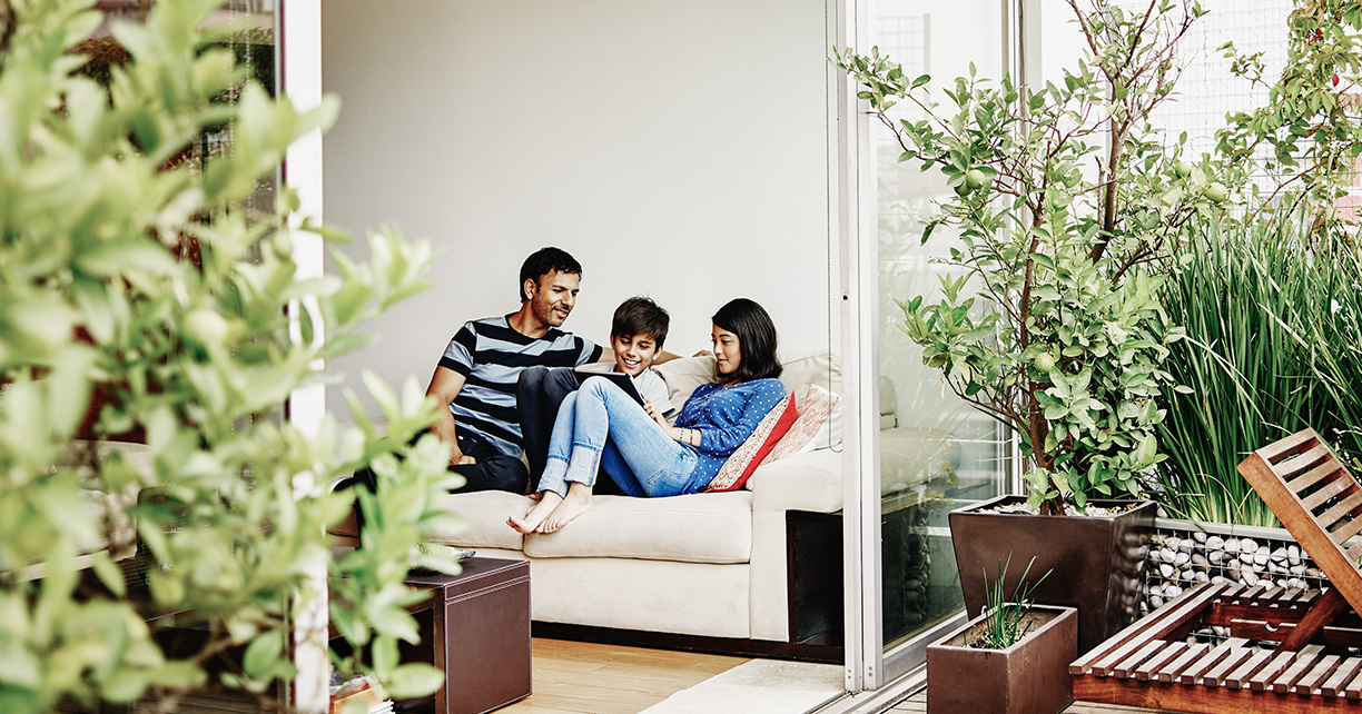 Smiling family sitting together on sofa in home looking at digital tablet