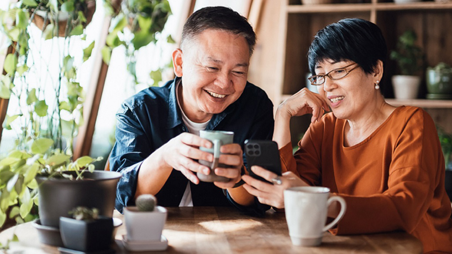 Happy senior Asian couple video chatting, staying in touch with their family using smartphone together at home. Senior lifestyle. Elderly and technology