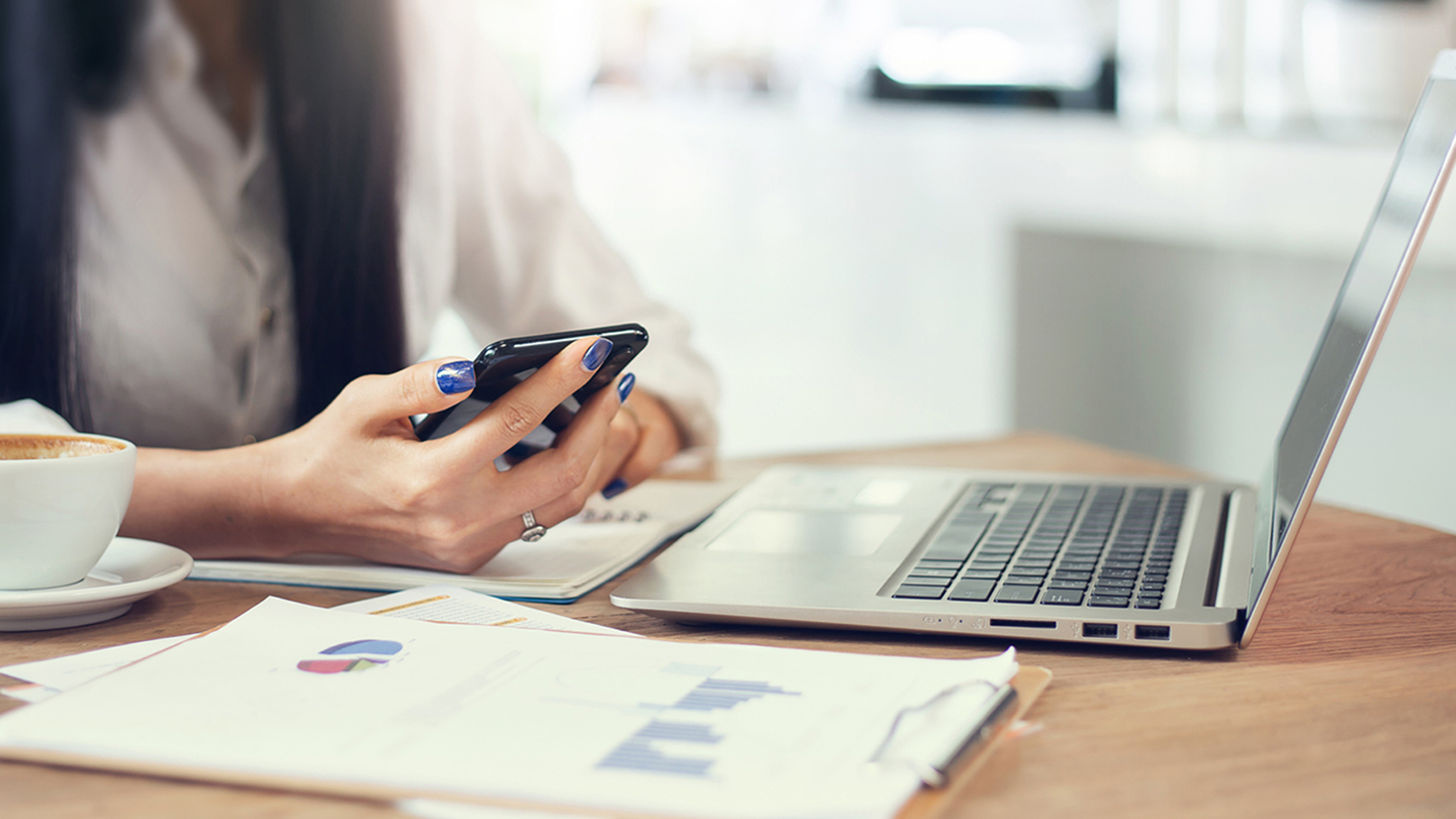 Focus on hand, young asian businesswoman using mobile phone and laptop computer working online  with paperwork and chart