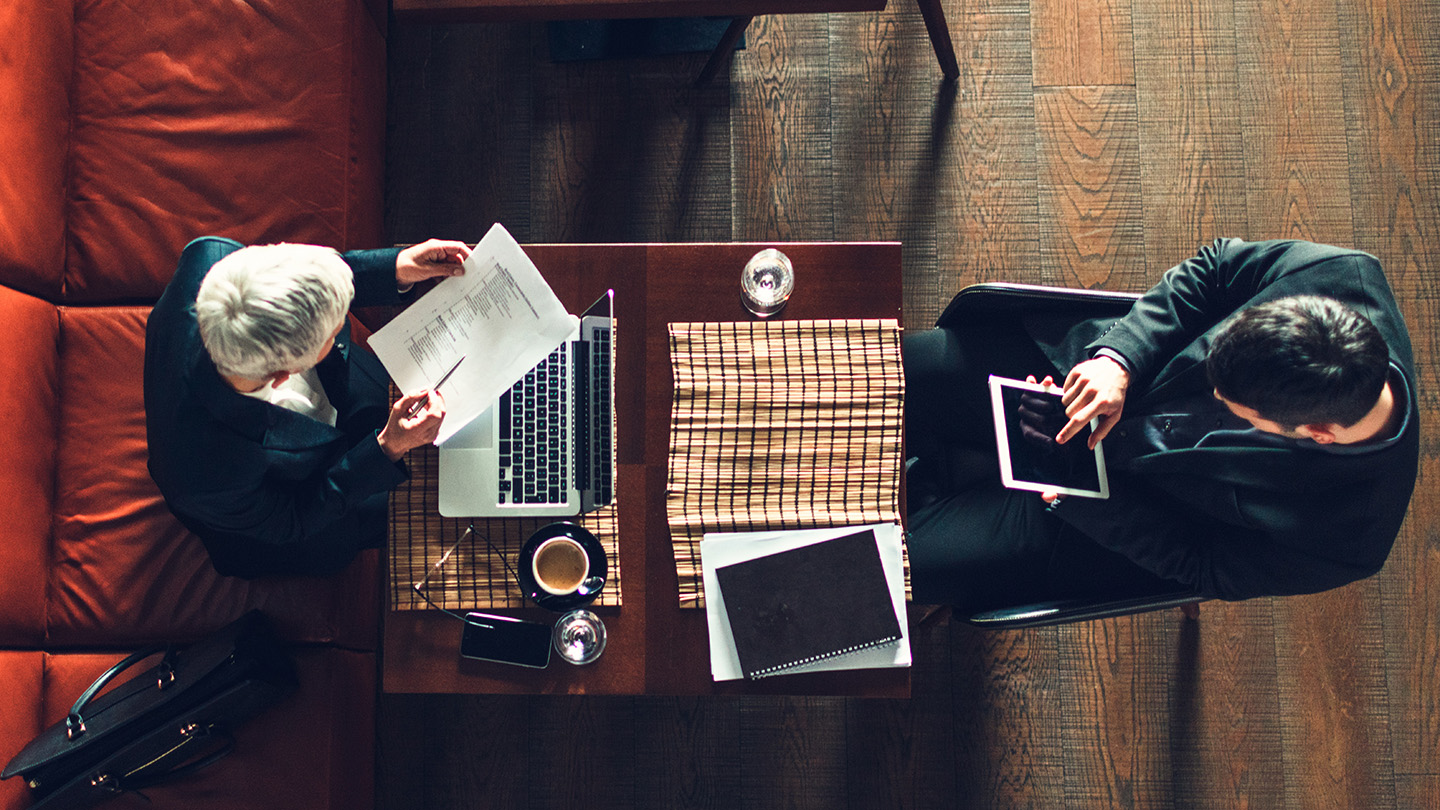 Businesspeople sitting in restaurant and having meeting. They are examining documents, finishing their paperwork. In front of mature businesswoman is laptop. Overhead view.