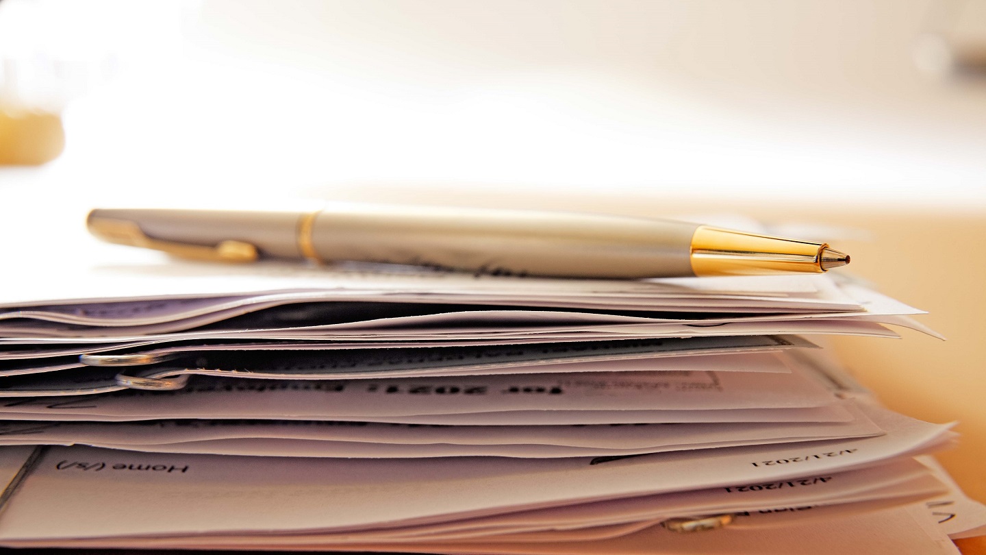 A ballpoint pen rests on top of a random stack of documents held together by paper clips.  Photographed with a very shallow depth of field.