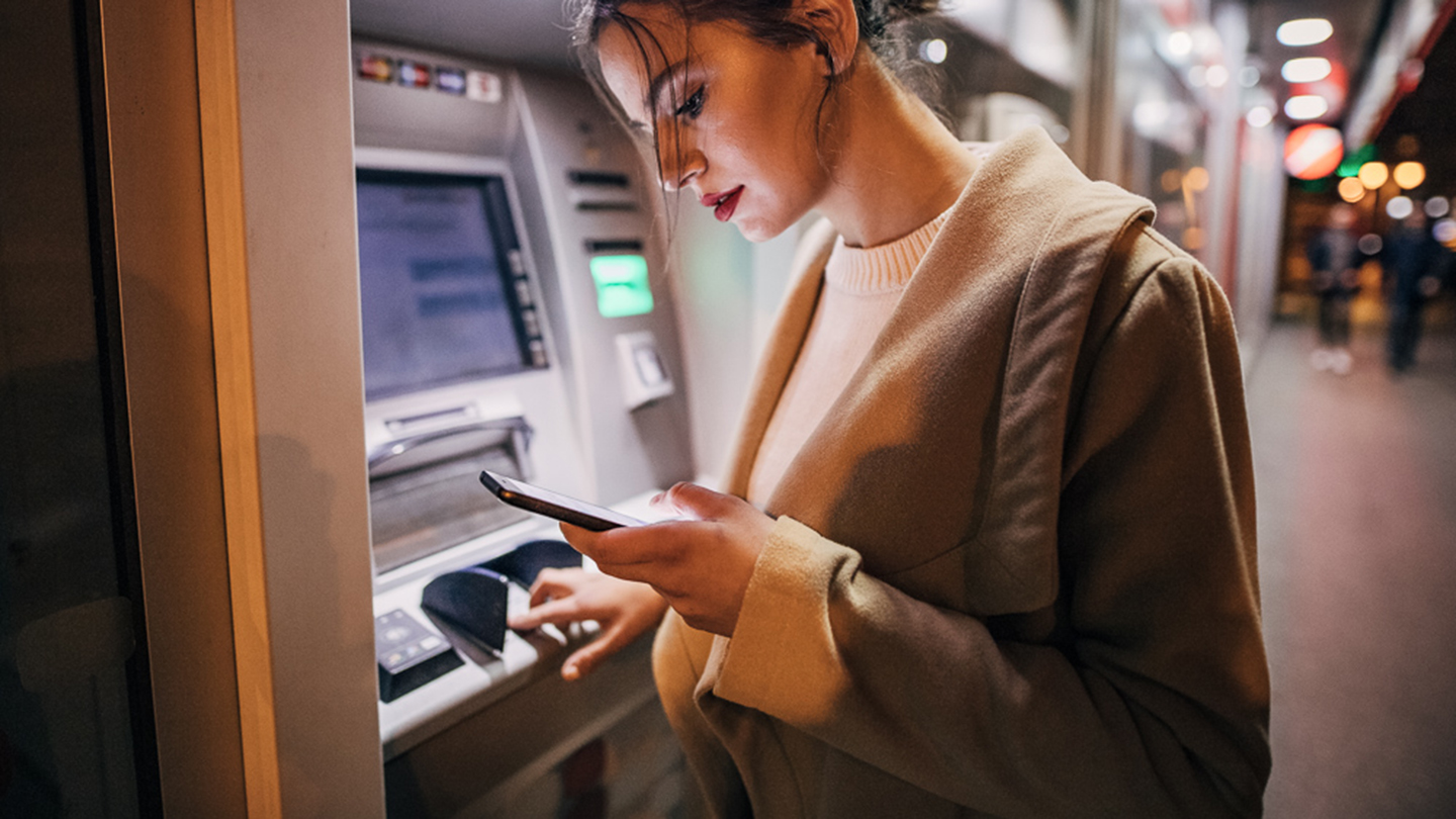 One young beautiful young teenage girl using ATM machine and smart phone in the city