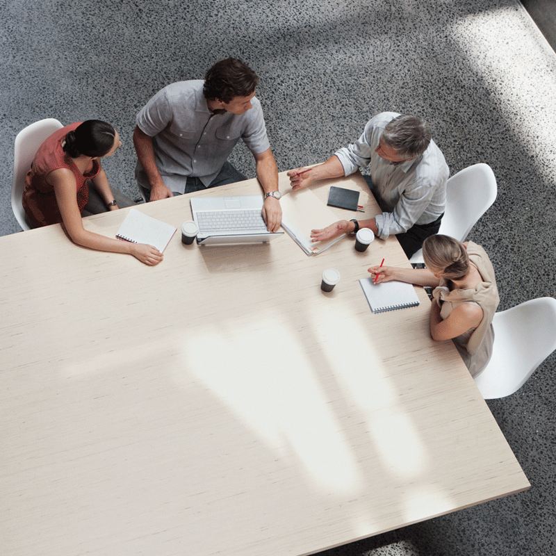 Aerial view of people with laptops and paper having a meeting at a conference table