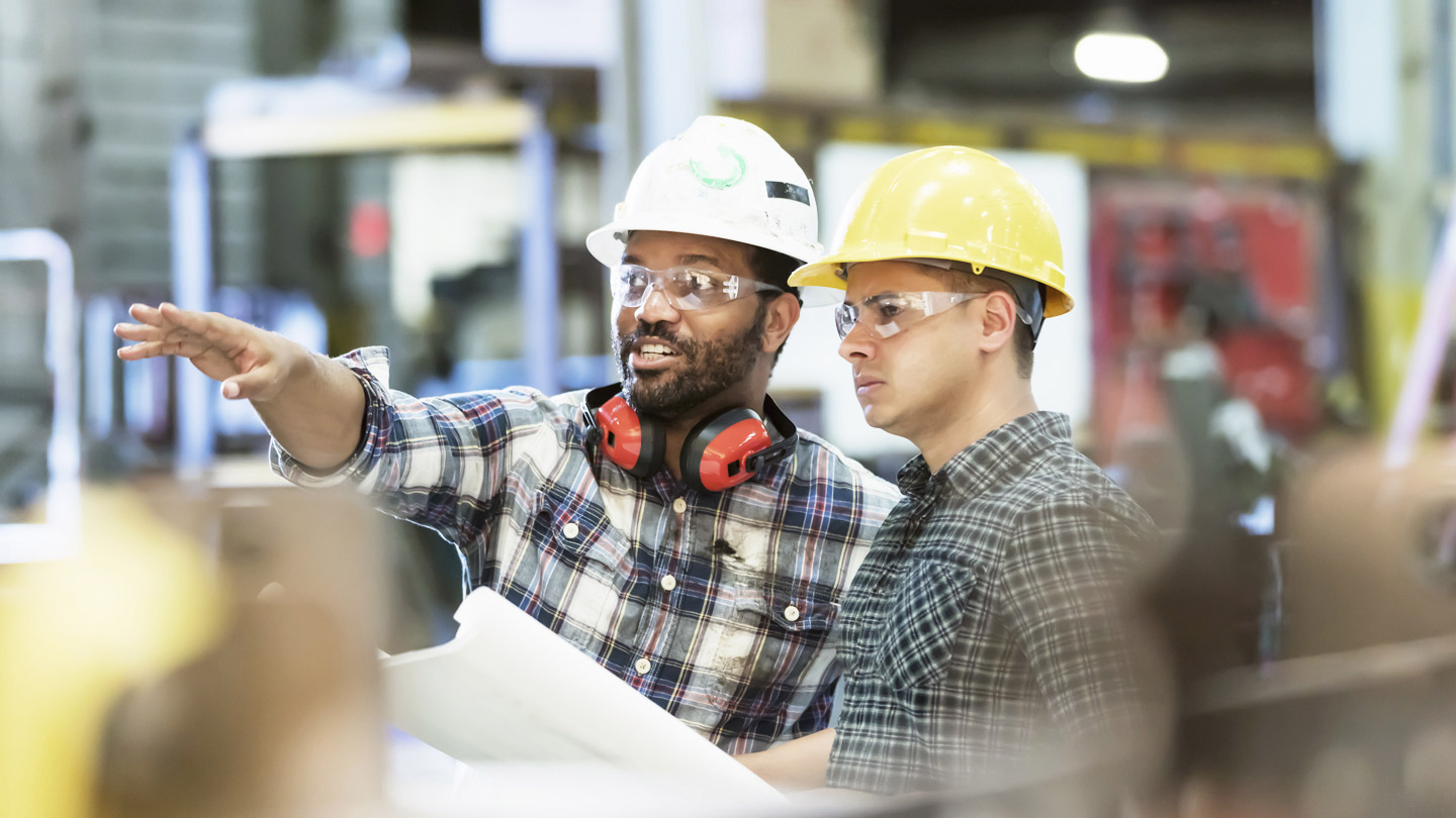 Two construction workers looking at blue prints and pointing in the distance