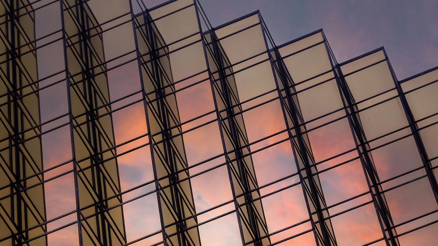 Glass building facade with geometric patterns reflecting a colorful sunset sky