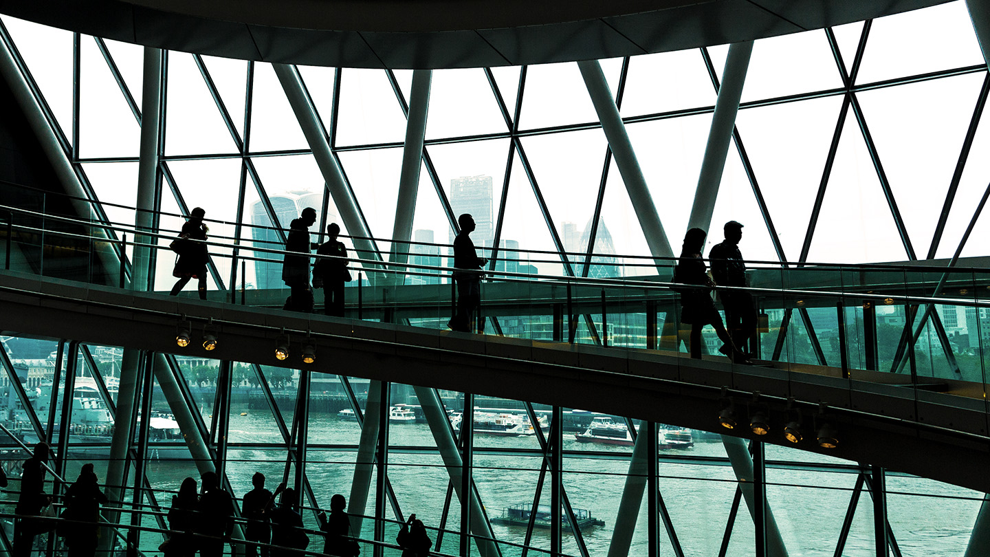 Silhouettes of people walking down a ramp with a window view of a river