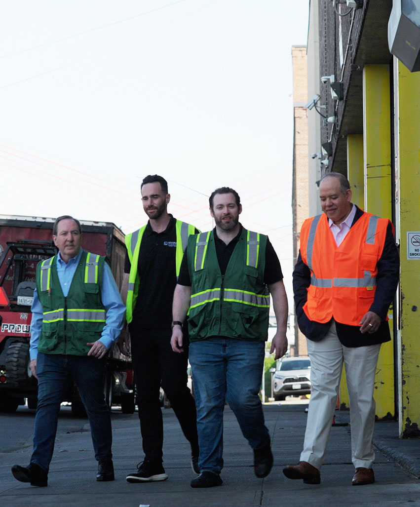People in safety vests walking outside an industrial facility.