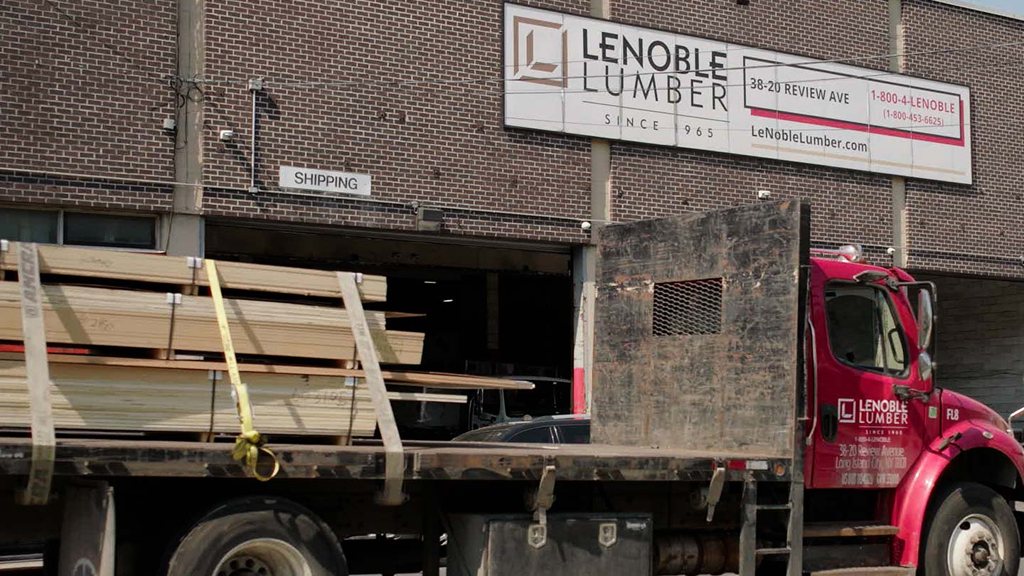 Lumber truck loaded with wood outside a warehouse loading dock.