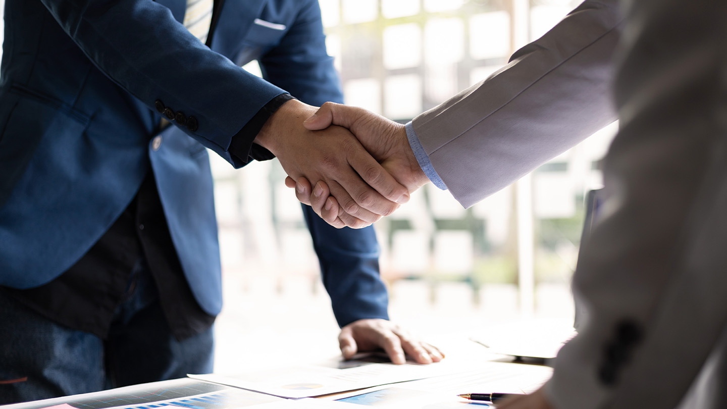 Two business professionals shaking hands over a desk, symbolizing agreement or partnership.
