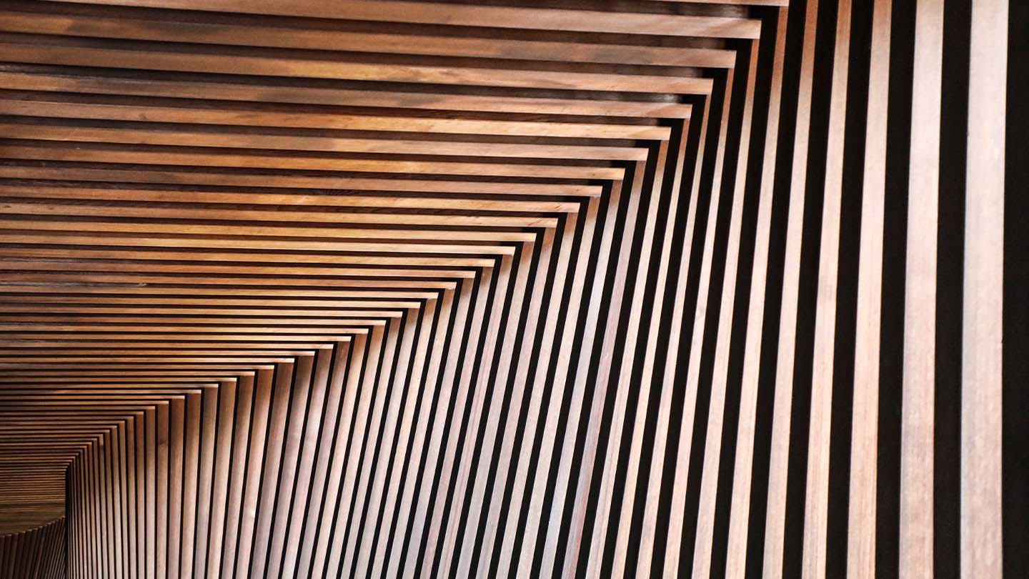 Abstract geometric pattern of repeating wooden slats forming a tunnel-like perspective with converging lines.