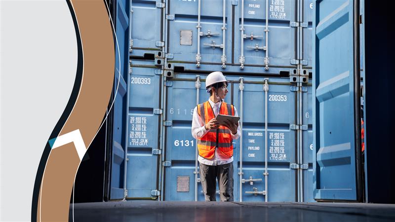  A worker in a safety vest and helmet inspects shipping containers with a tablet at a logistics facility.