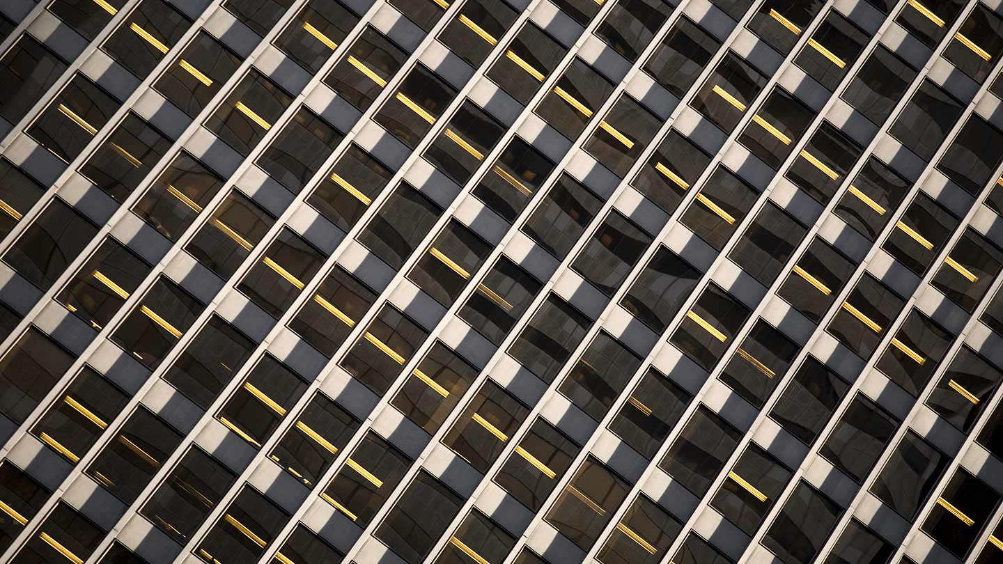 Diagonal view of a modern building facade with repeating windows and yellow lights.