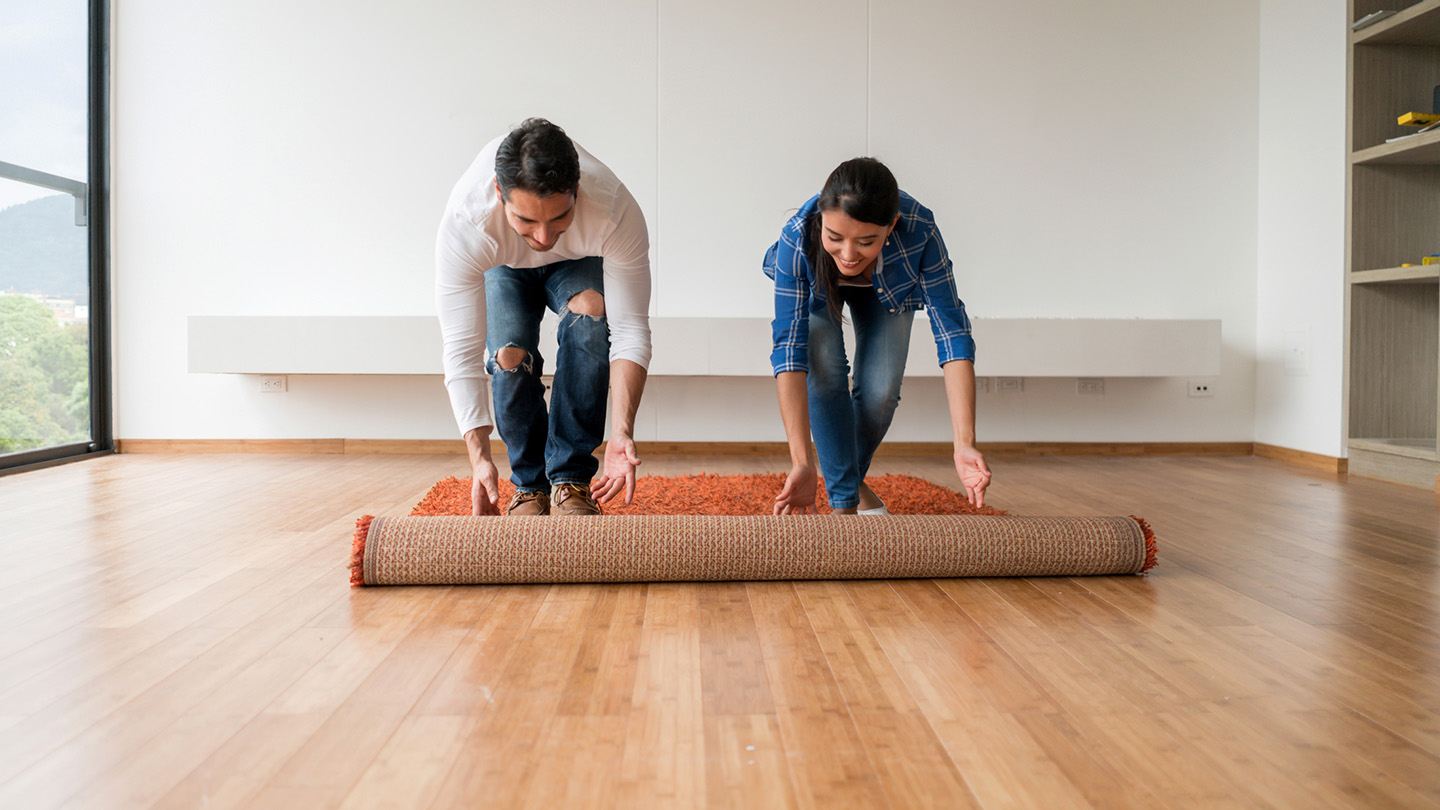 A couple rolls out a rug in their new apartment