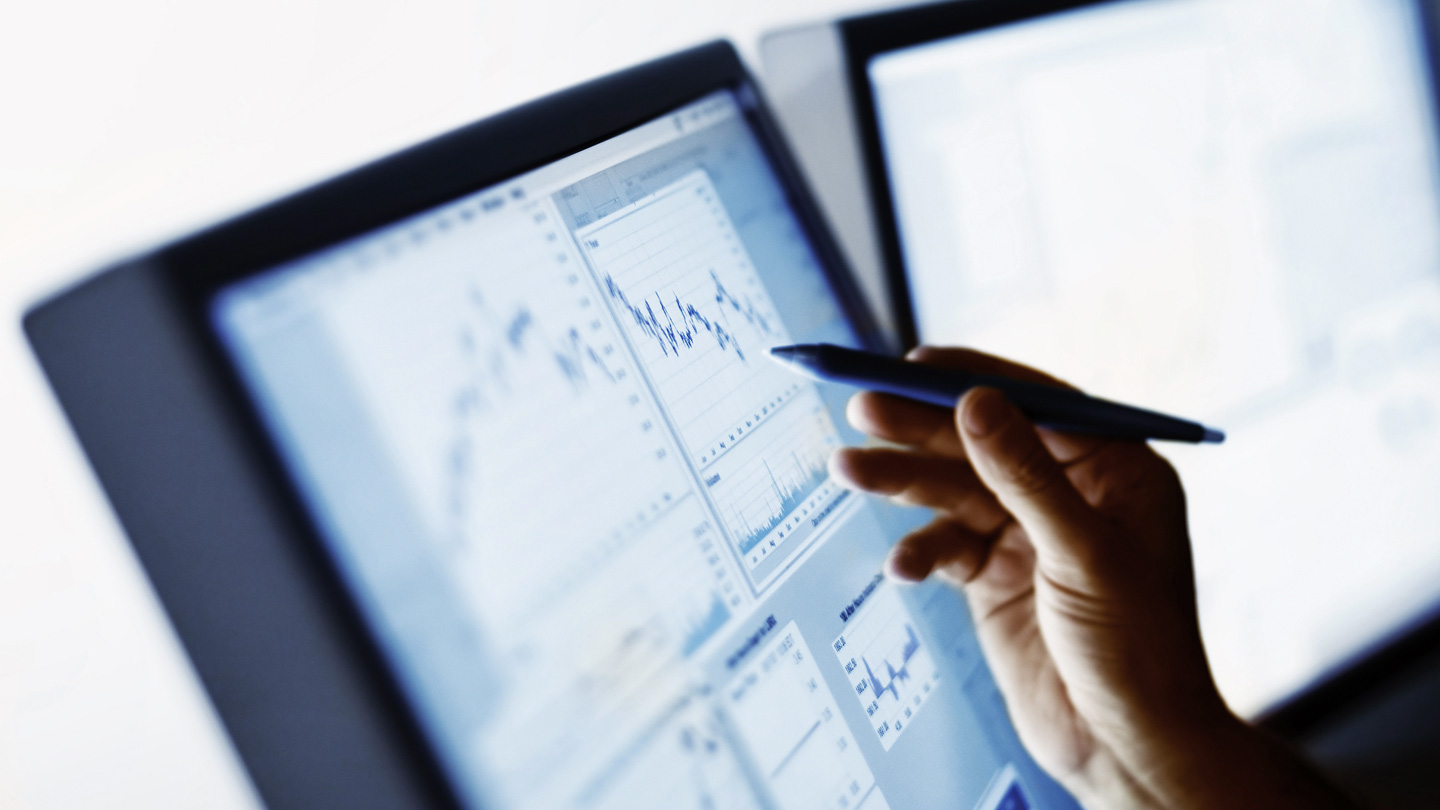 Person holds a pen while examining charted data on a computer screen