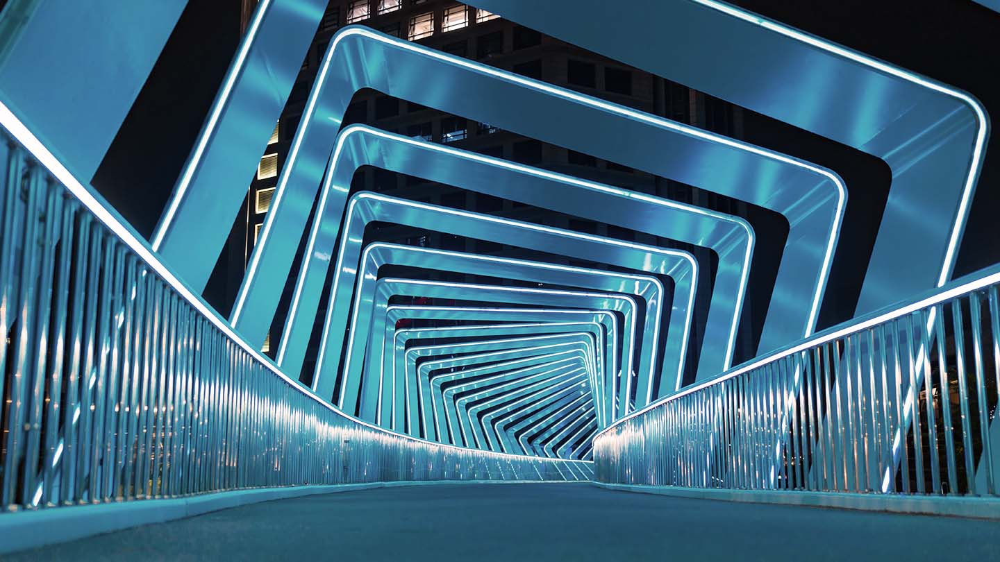 Blue-lit geometric frames forming a tunnel over a pedestrian bridge at night