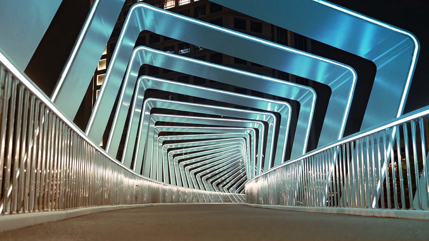 Illuminated blue rectangular frames forming a tunnel along a pedestrian bridge at night