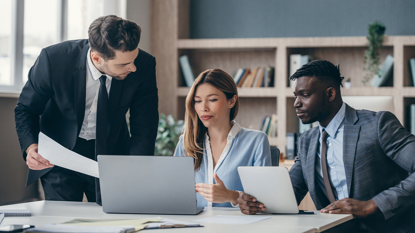3 people in a meeting using a laptop and tablet