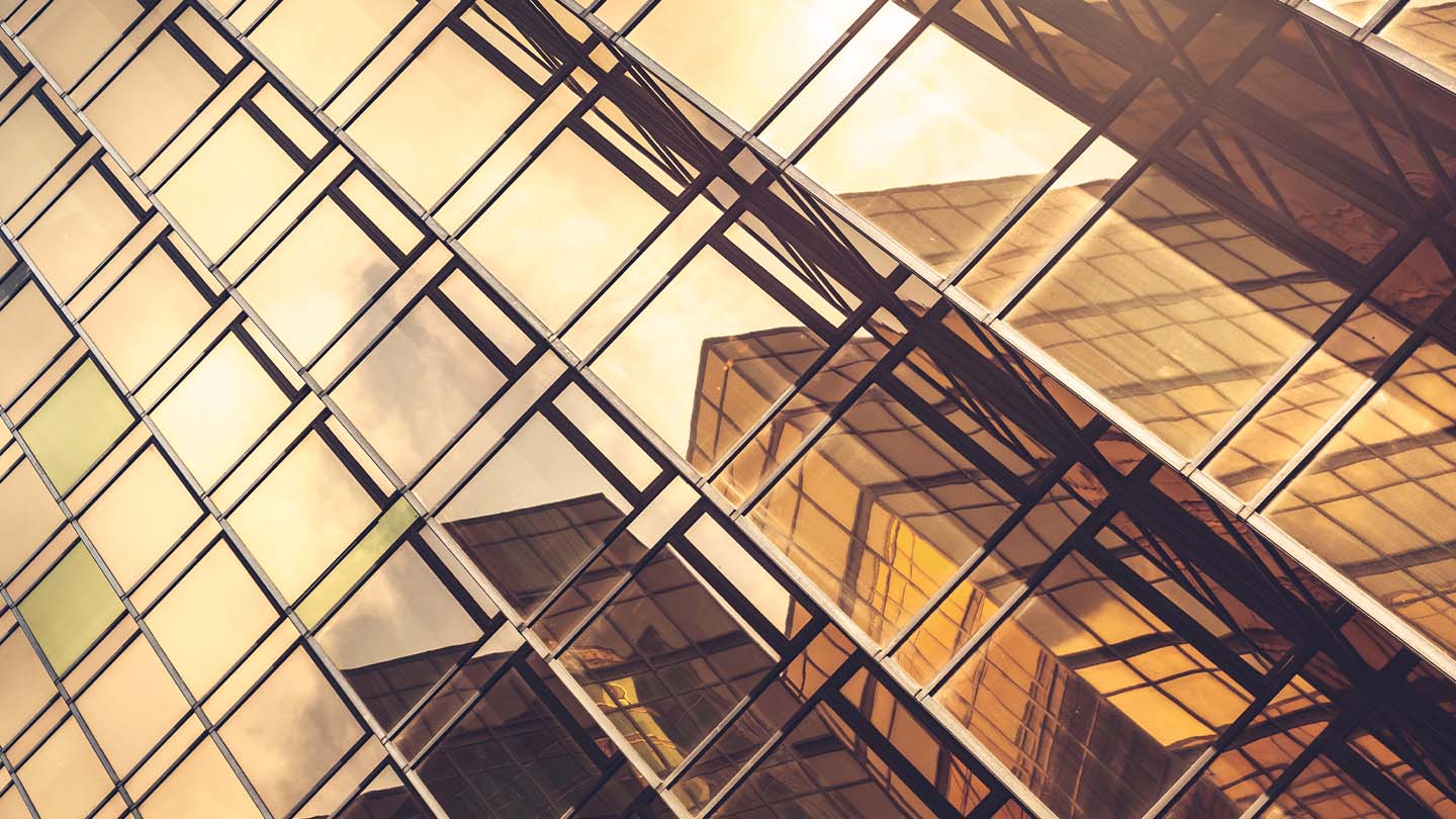 Glass building facade reflecting geometric patterns and warm sunlight.