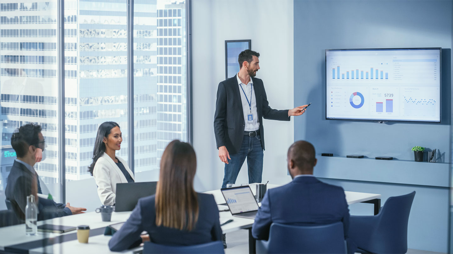 A business professional presents data charts on a screen to colleagues in a modern conference room