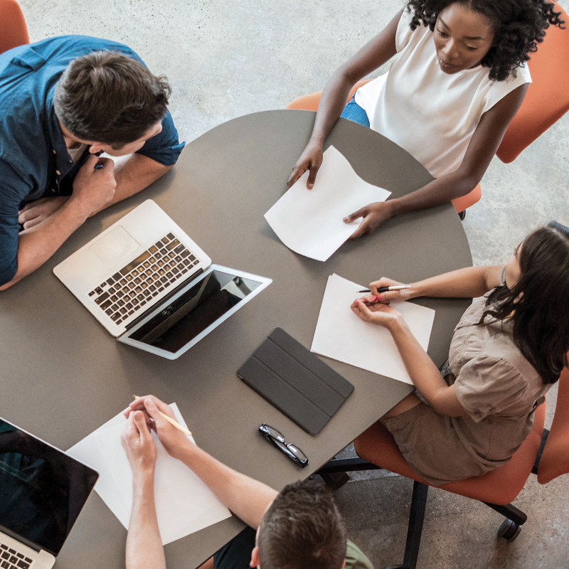 Aerial view of group sitting at table with papers and laptops talking