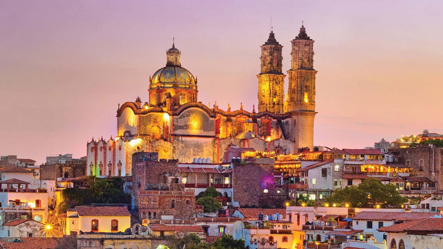 Illuminated historic church overlooking a town at sunset.