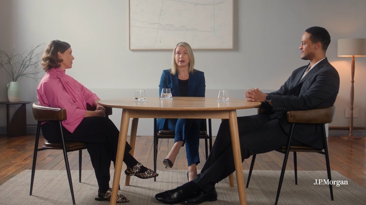 Three people sit around a wooden table in a meeting room, with the “J.P. Morgan” watermark in the lower-right.