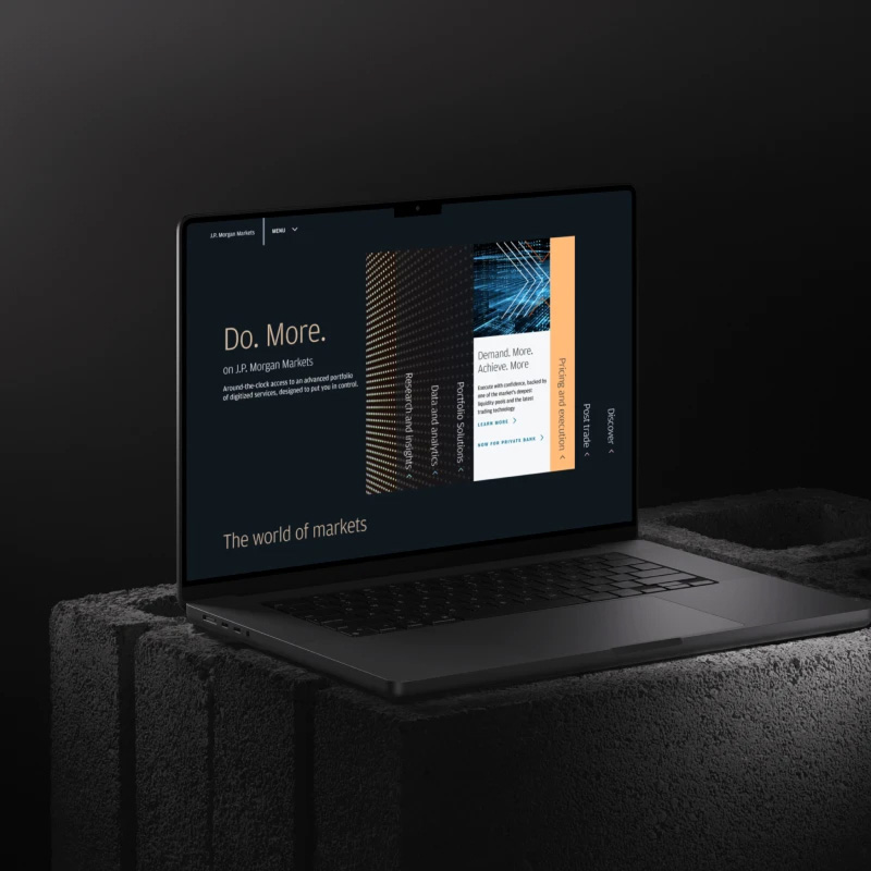 Laptop on a dark textured surface displaying a markets webpage with the headline “Do. More.” on screen.