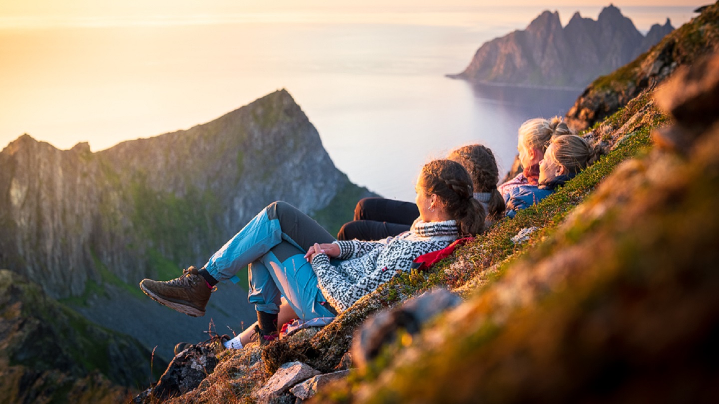 Friends relaxing together at sunset lying down on mountain ridge, Senja island, Troms county, Norway