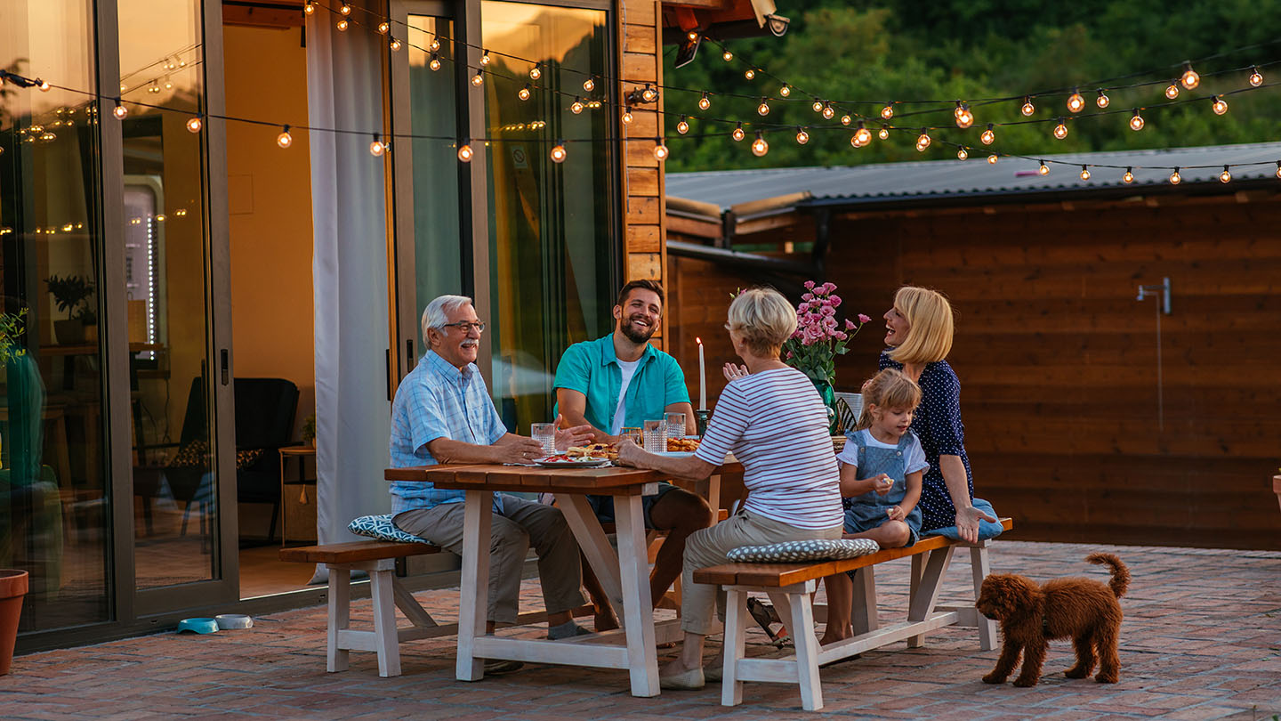 Happy family eating together outdoors. Smiling generation family sitting at dining table during dinner. Happy cheerful family enjoying meal together in garden.