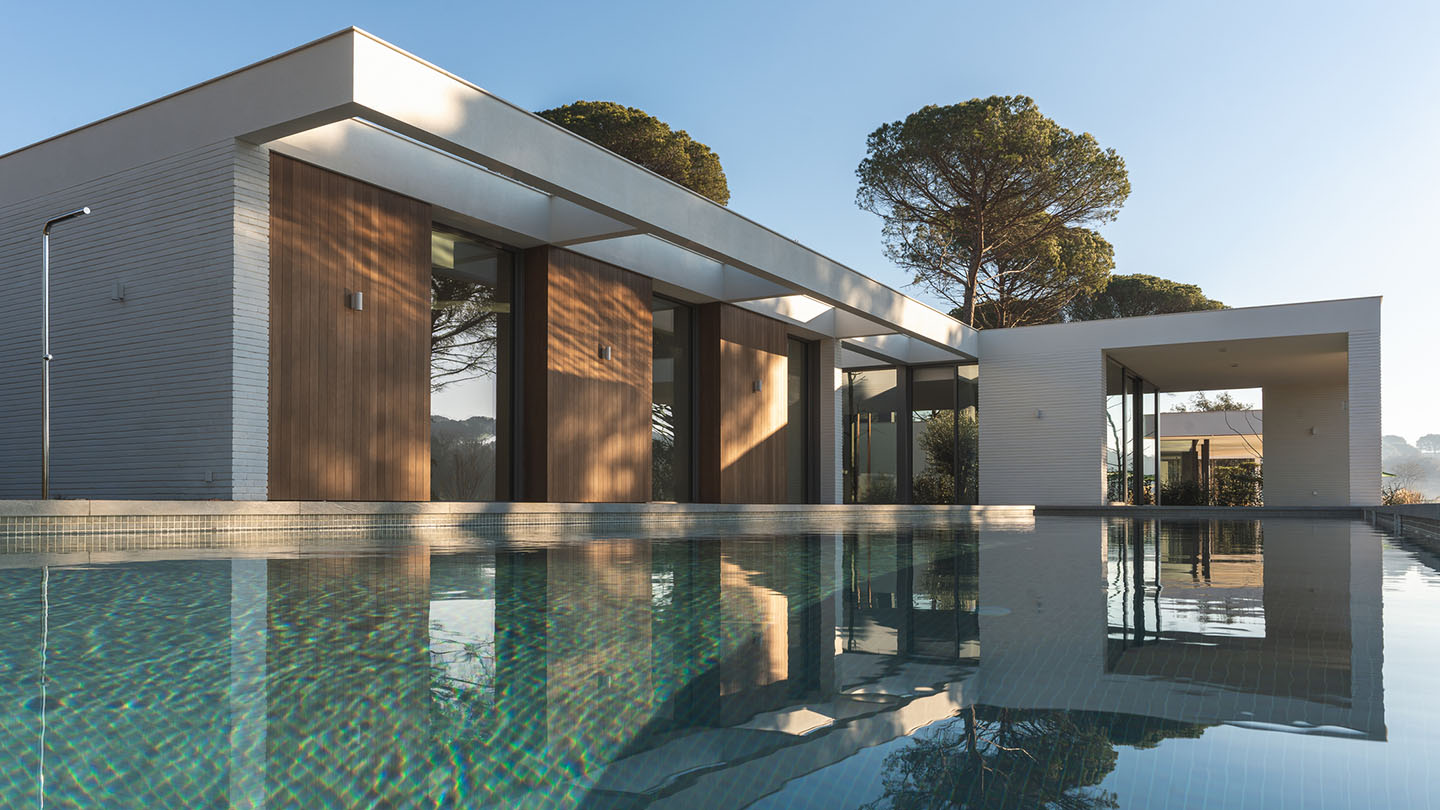 Modern white and wood house with pool and pine trees outside.