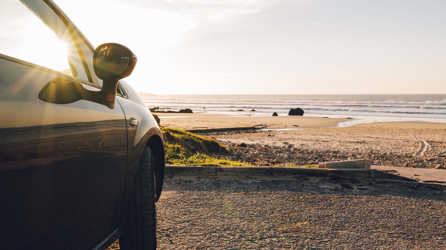 A car parked by a beach at sunset