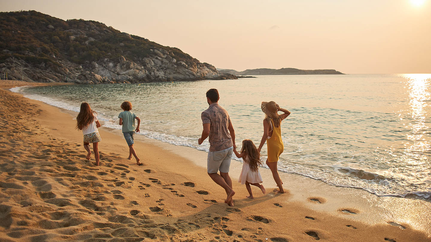 A family run hand in hand down a tropical paradise beach during sunset.