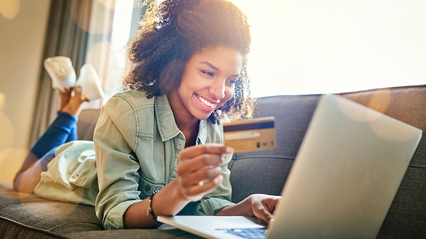 Shot of a cheerful young woman doing online shopping while lying on a couch at home during the day