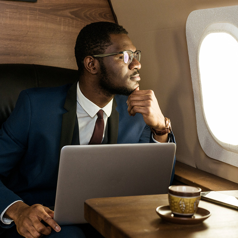 Attractive and successful African American businessman with glasses working on a laptop while sitting in the chair of his private jet.; Shutterstock ID 1376572913; Job: -; purchase_order: -; client: -; other: -