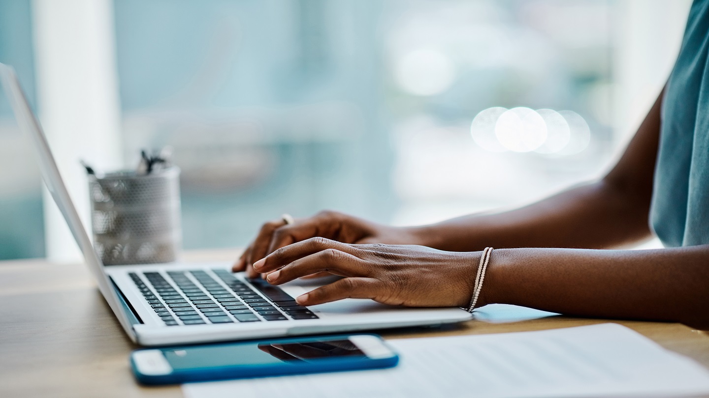 Closeup of a black businesswoman typing on a laptop keyboard in an office alone