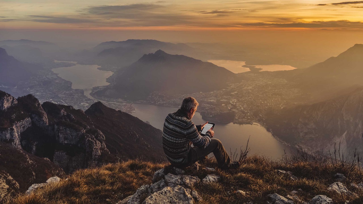 Man hiker solo on the mountain during golden hour reading e-book
