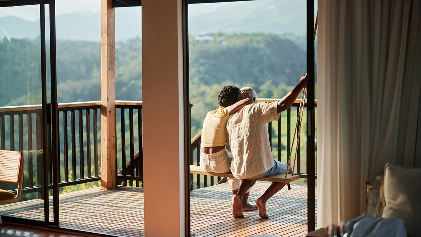 Rear view of a loving couple sitting on a swing on the balcony of their vacation rental and looking at the scenic view
