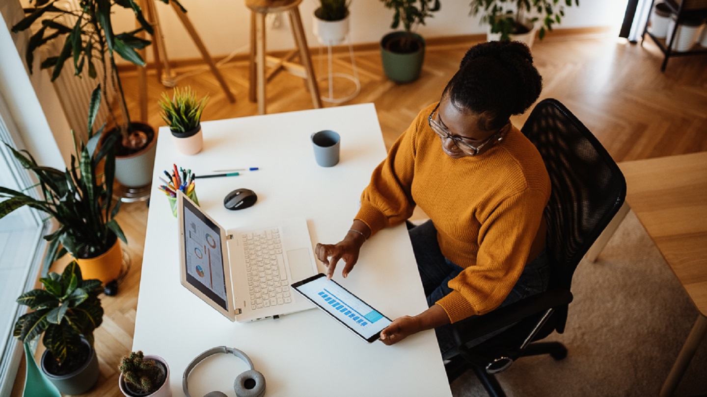 Young African businesswoman dressed in earthly toned clothing working on laptop